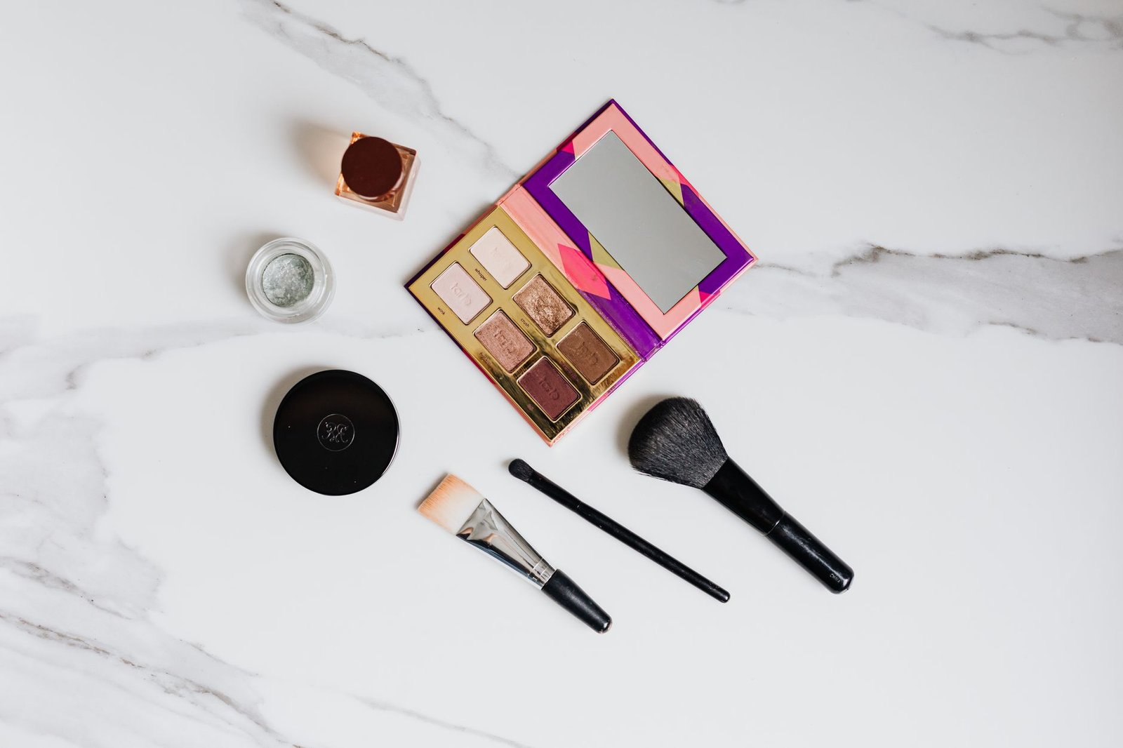 Flat lay of makeup brushes and eyeshadow palette on marble