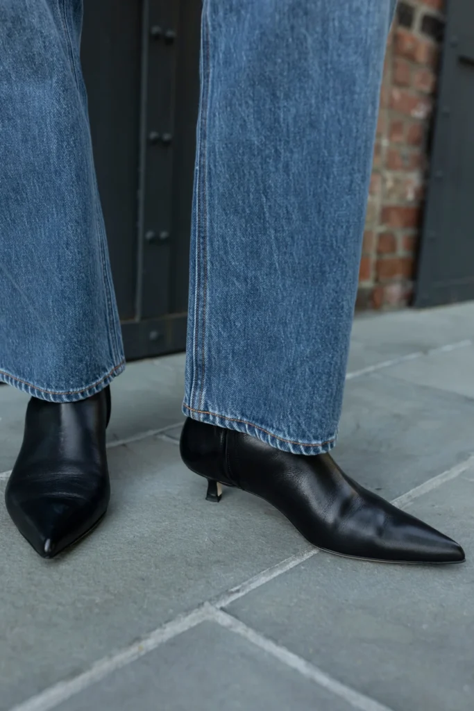 Black pointed-toe ankle boots styled with wide-leg blue jeans