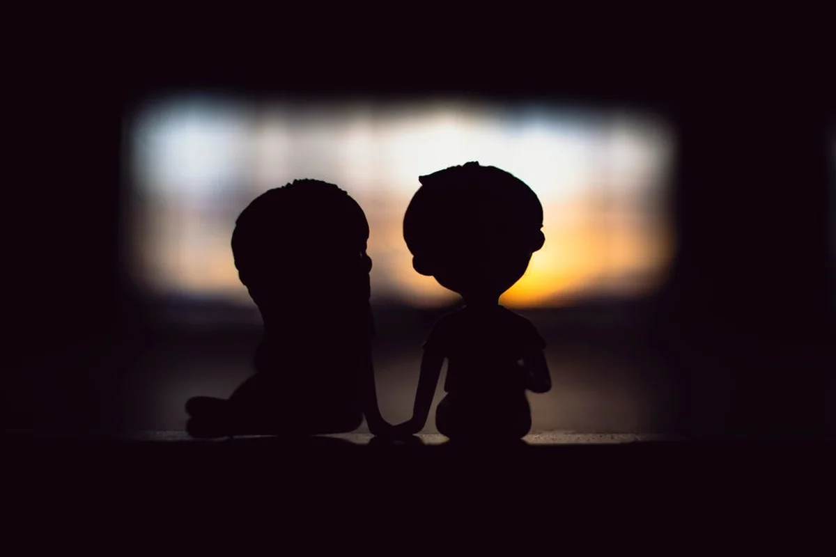Two silhouetted figures holding hands by a window at dusk