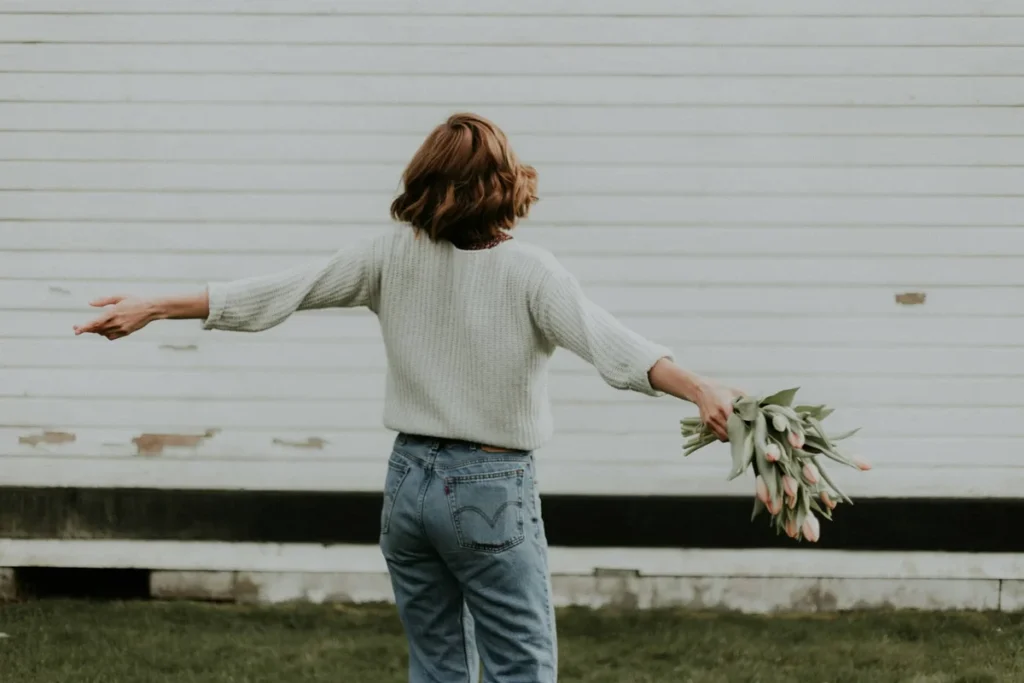 Woman seen from behind holding tulips by a white barn wall