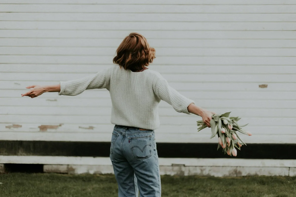 Woman seen from behind holding tulips by a white barn wall